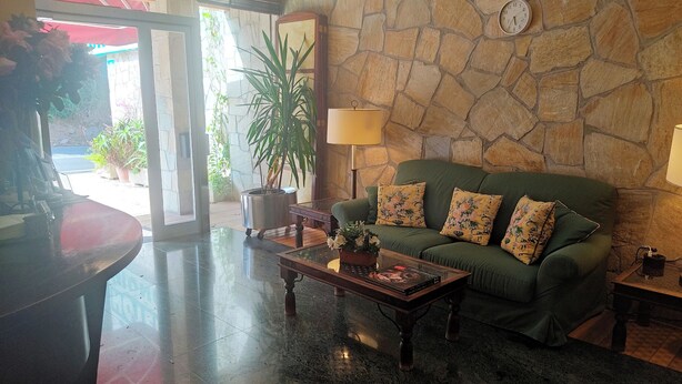 A living room with a stone wall, a green sofa with floral cushions, a wooden coffee table, and a potted plant. - Hotel Suite Mioño Castro  (Castro Urdiales)
