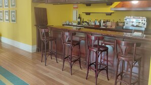 A bar area with wooden bar stools, a countertop with various bottles, and a coffee machine. - Hotel Suite Mioño Castro  (Castro Urdiales)