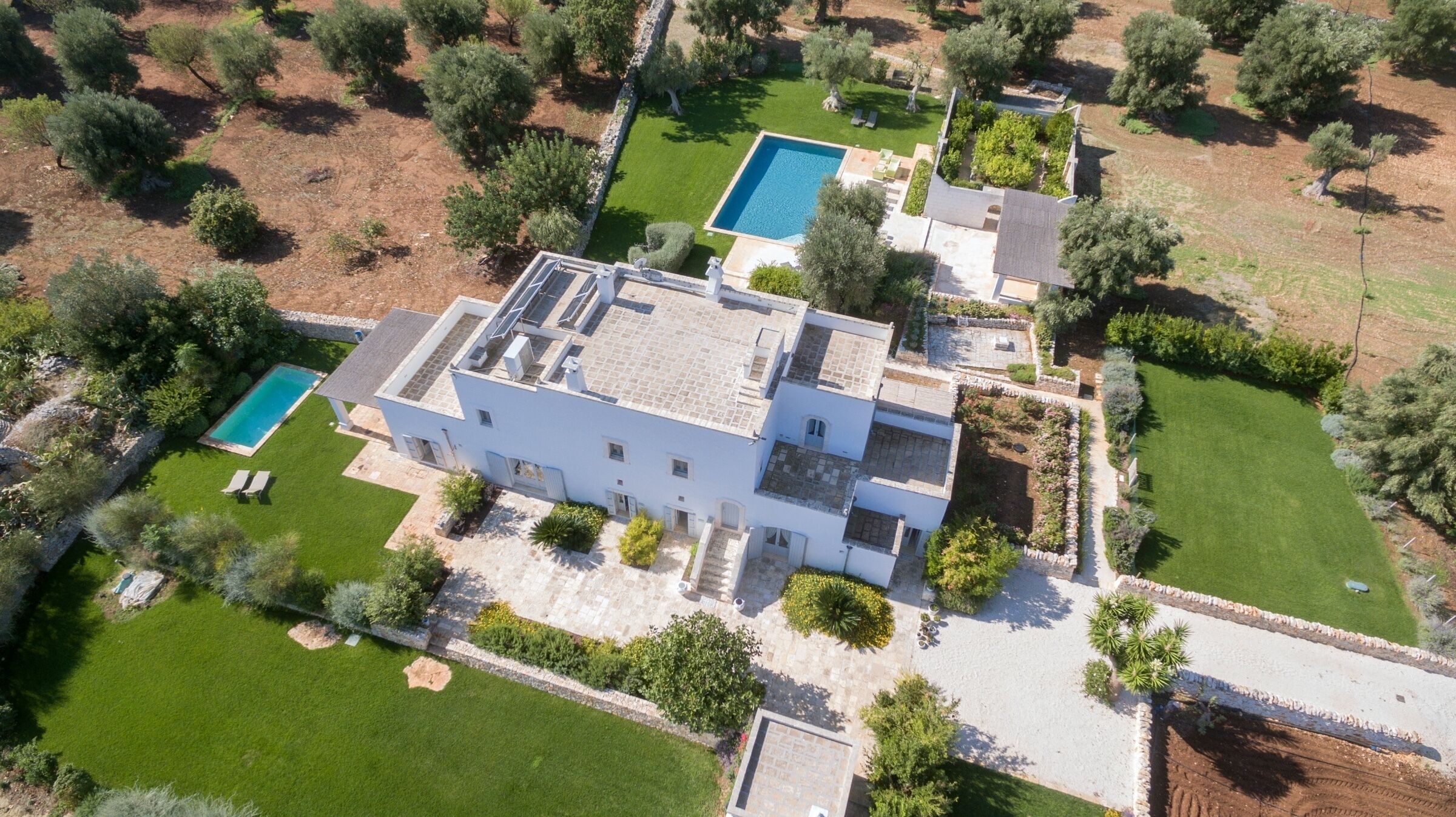 An aerial view of a modern two-story house with a swimming pool, a well-maintained lawn, and surrounding vegetation.