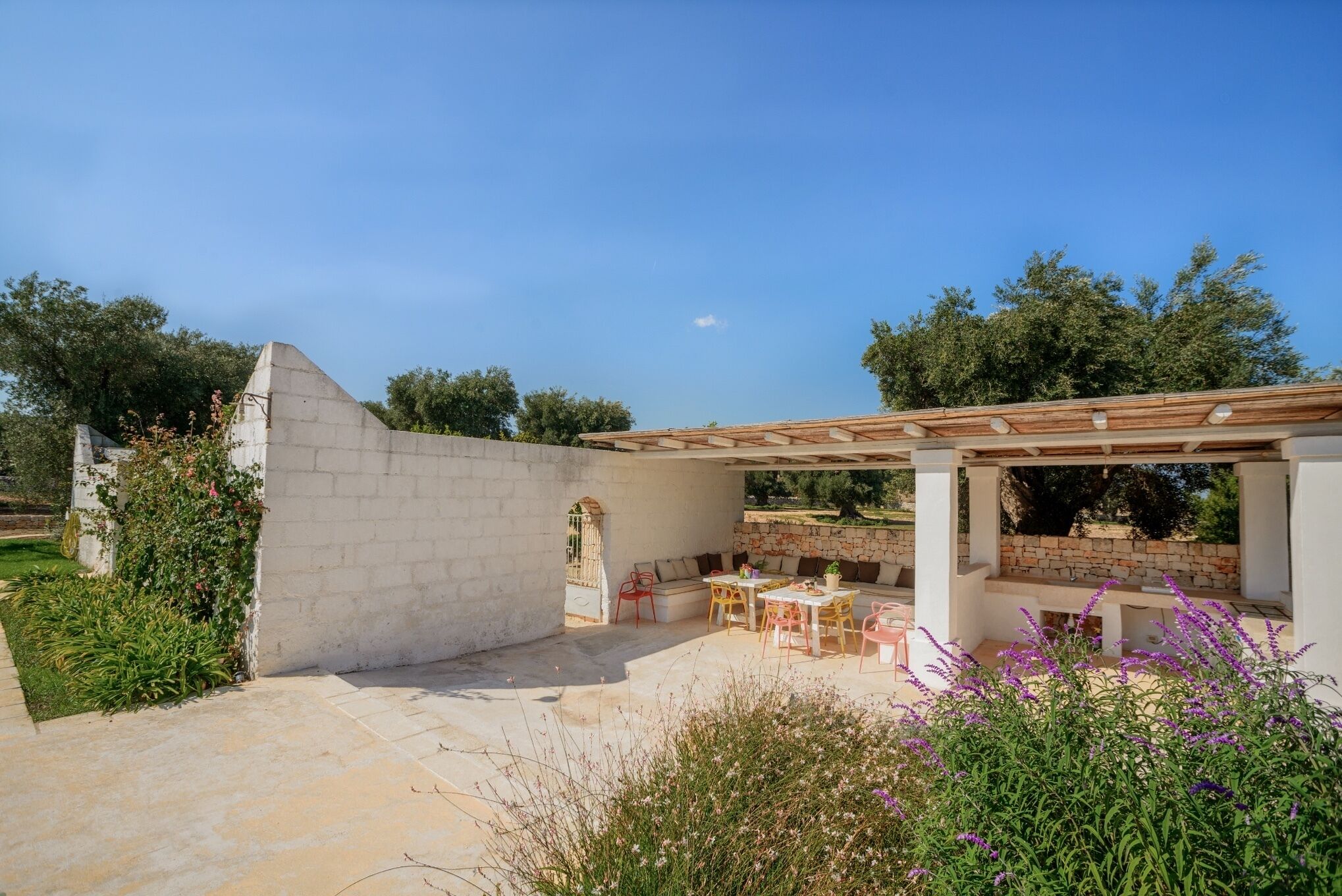 An outdoor patio area with a stone wall, a pergola, and seating arrangements.