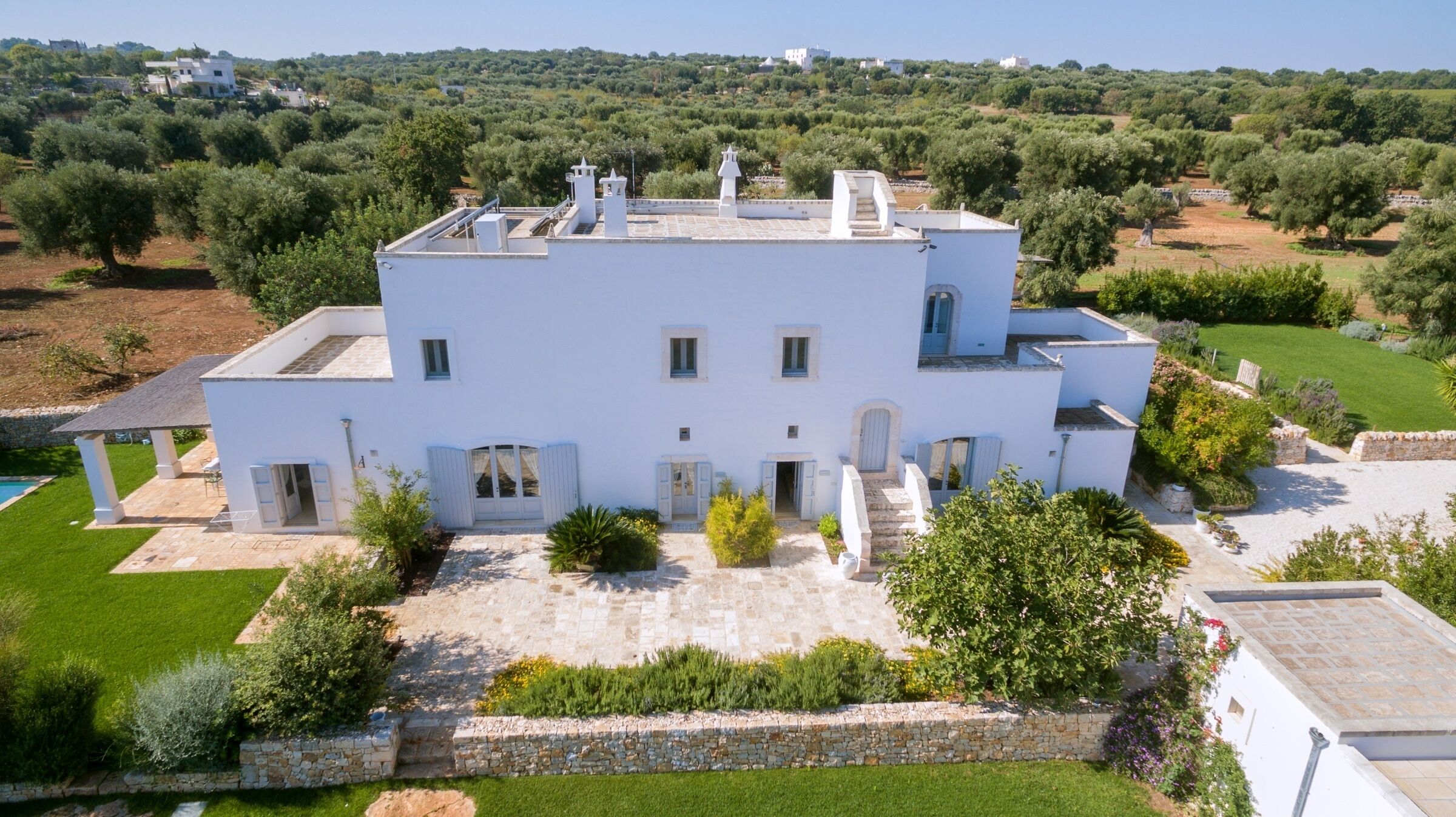 A white villa with a spacious courtyard, multiple windows, and a pool.