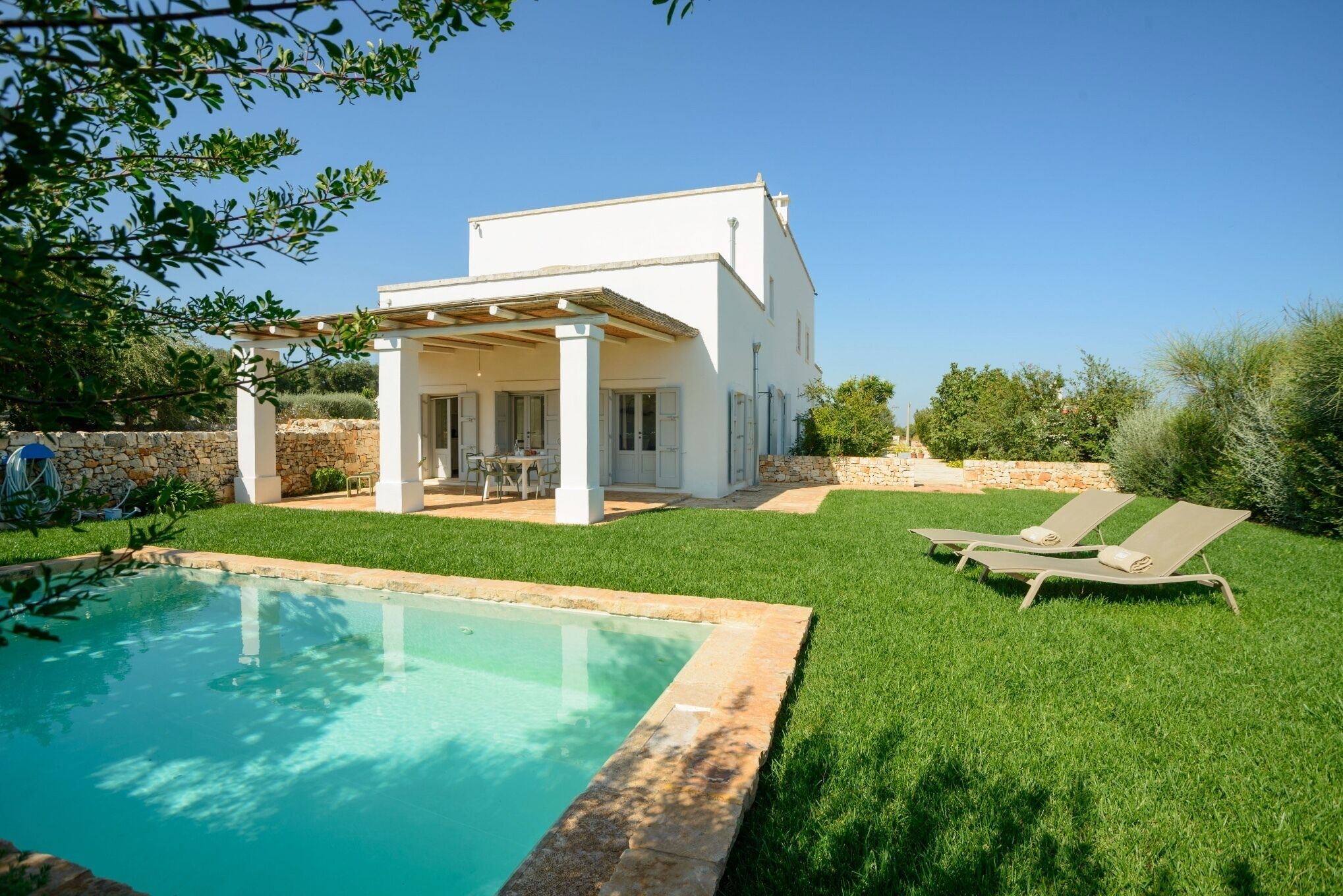 Una casa moderna con piscina, patio y dos sillones de descanso.