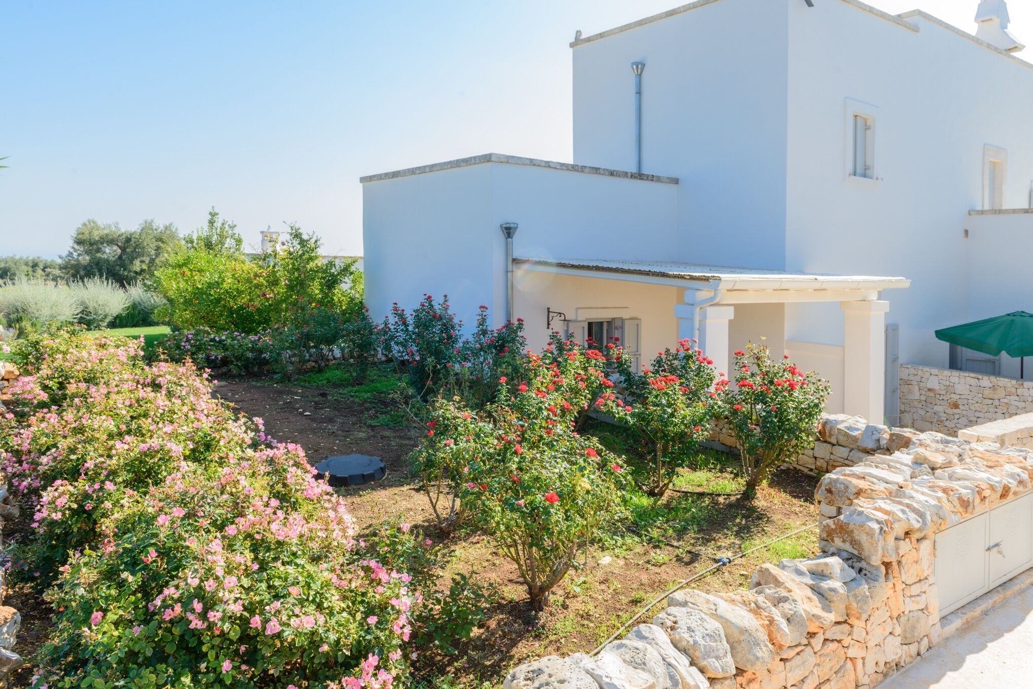 Ein weißes Gebäude mit einer Steinwand und einem Garten mit rosa und roten Blumen.