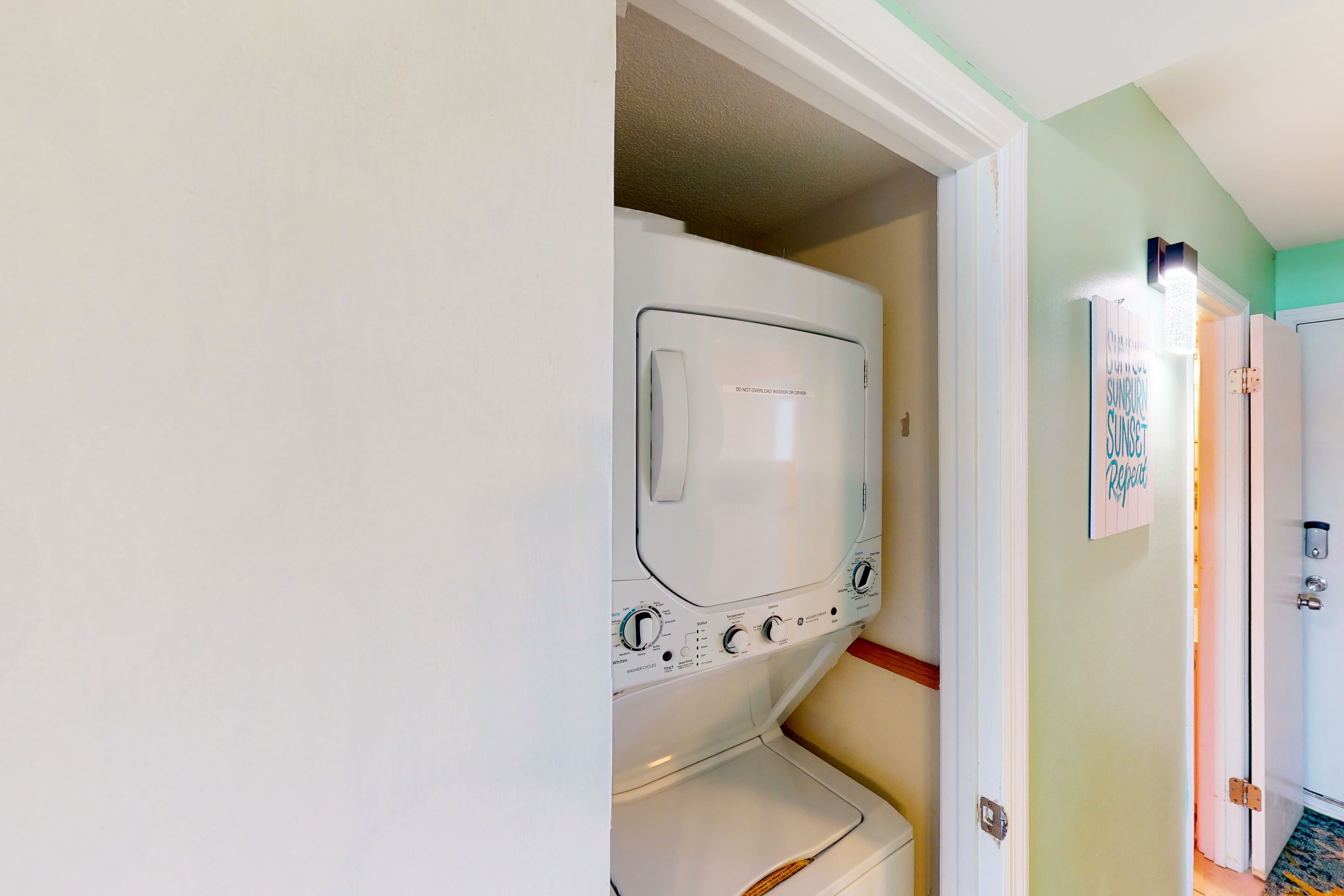 A laundry room with stacked washers and dryers, a door with a sign, and a light fixture above the door.