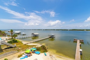 A waterfront property with a dock extending into the water, a sandy beach area with kayaks, and a clear view of the water. - Summer House West Condos (Gulf Shores)