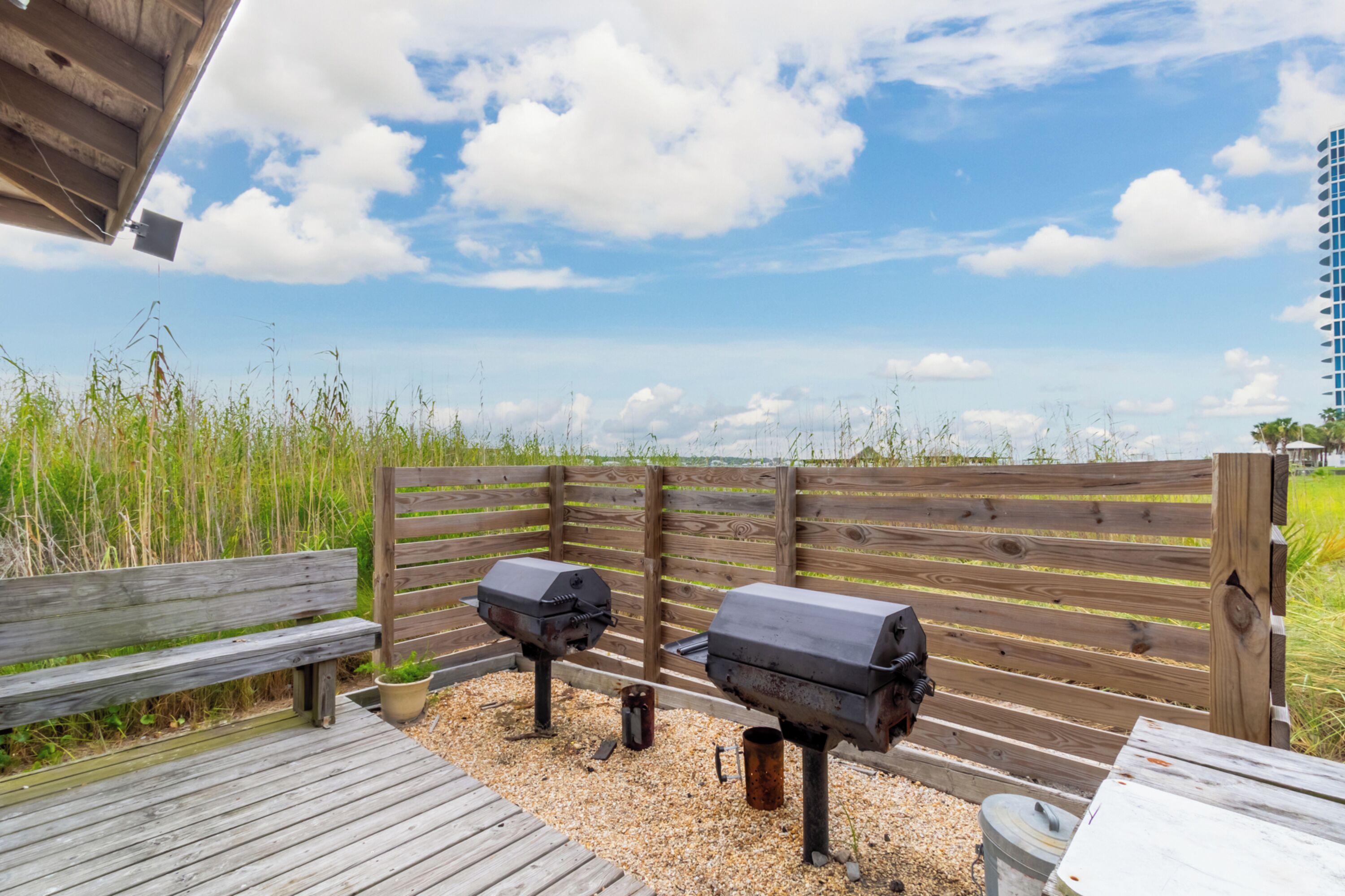 Une terrasse en bois équipée de deux barbecues, d’un banc en bois et offrant une vue sur la plage et l’océan.