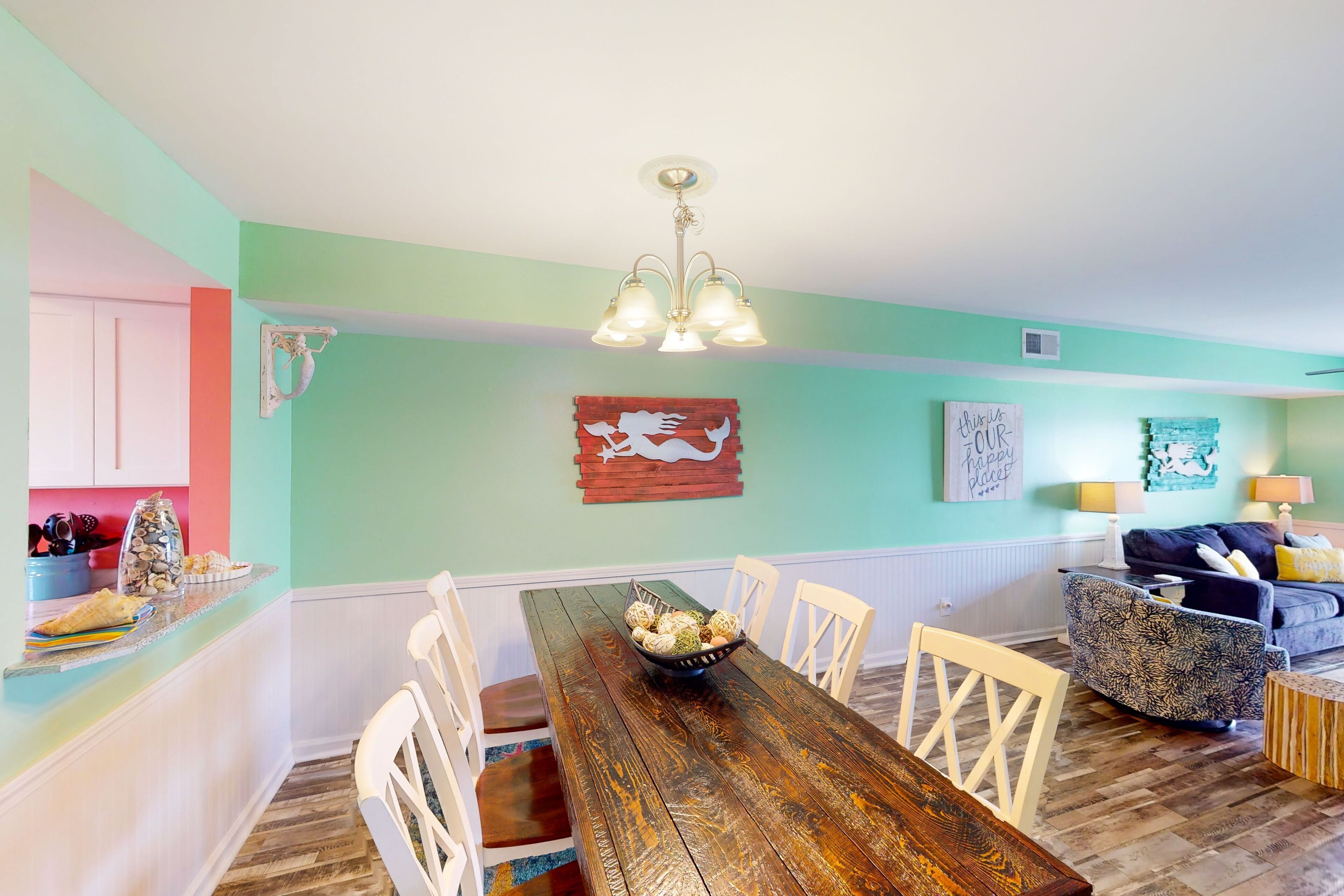 Un coin repas avec une table en bois, des chaises blanches et une décoration murale.