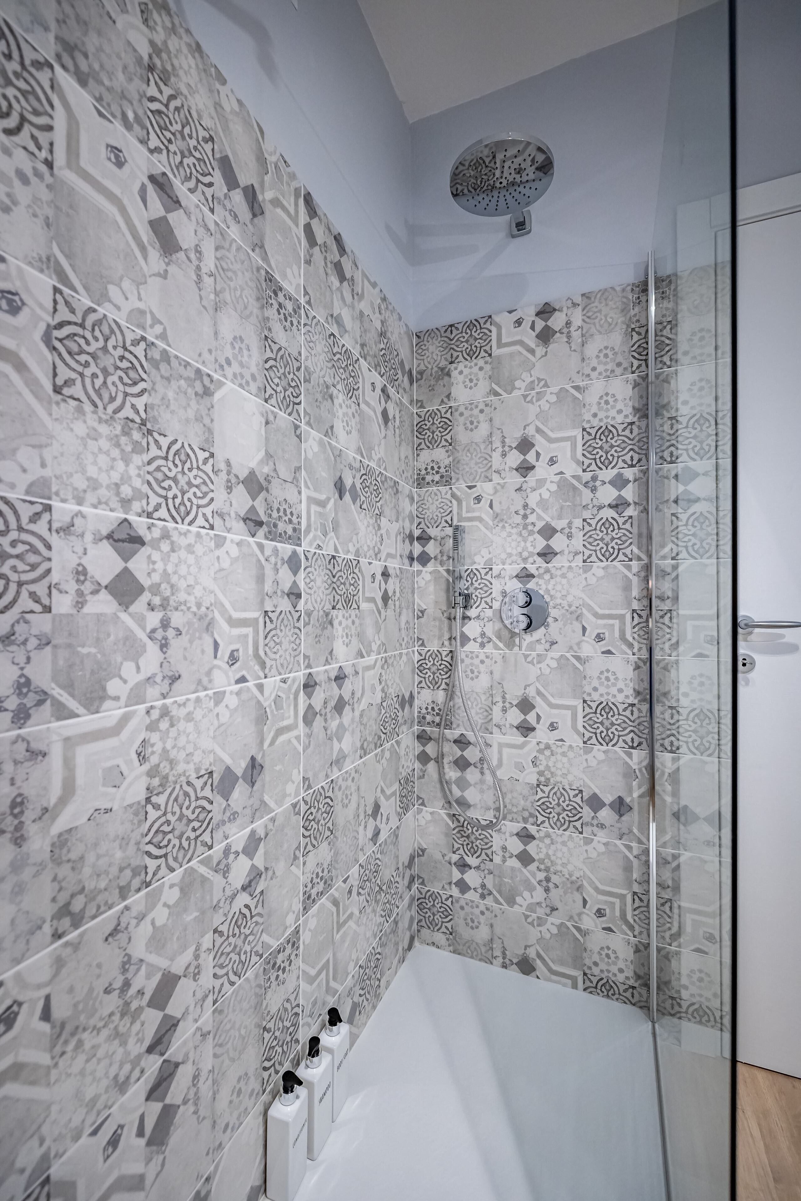 A bathroom with patterned tiles, a glass shower enclosure, and a white bathtub.