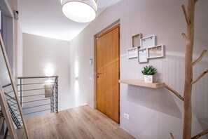 Un couloir avec une porte en bois, un escalier et une étagère fixée au mur, sur laquelle est posée une plante en pot.
