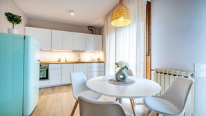 A modern kitchen with white cabinets, a blue refrigerator, and a dining area with a round table and white chairs.