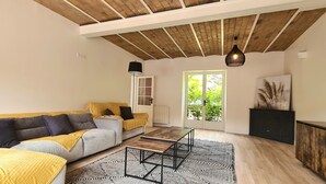 Uma sala de estar com um sofá, uma mesa de centro e um armário. Há uma porta com painéis de vidro e uma janela.