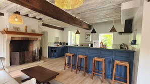 Uma sala de estar espaçosa com lareira, vigas de madeira, uma ilha grande com bancos e uma cozinha moderna.