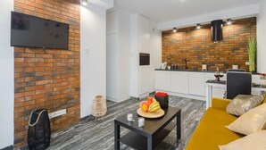 A modern living room with a flat-screen TV, a dining table with fruit, and a yellow sofa.
