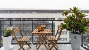 A balcony with a wooden table and chairs, a potted plant, and a bottle of wine.