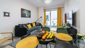 A modern living room with a green sofa, a dining table with yellow placemats, and a fruit bowl. - Lumina apart near Cinema Museum (Lódz)