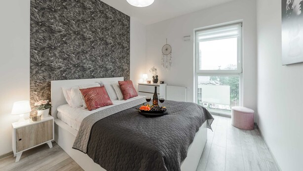 A modern bedroom with a large bed, a nightstand, a dresser, a window with a view, and a dreamcatcher on the wall. - Lumina apart near Cinema Museum (Lódz)