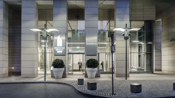Een modern gebouw met grote glasramen, een bord met 'Platinum Towers' en potplanten ervoor.