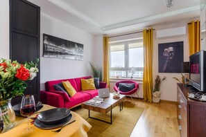 Een moderne woonkamer met een rode bank, een salontafel, een televisie en een groot raam met gordijnen.