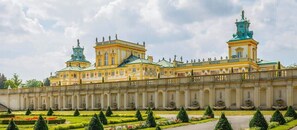 A large, classical building with symmetrical architecture, a central courtyard with geometrically shaped topiary, and a series of fountains along the building's facade.
