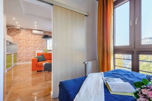 A modern room with a bed, a blue bedspread, a book, and a window with curtains.
