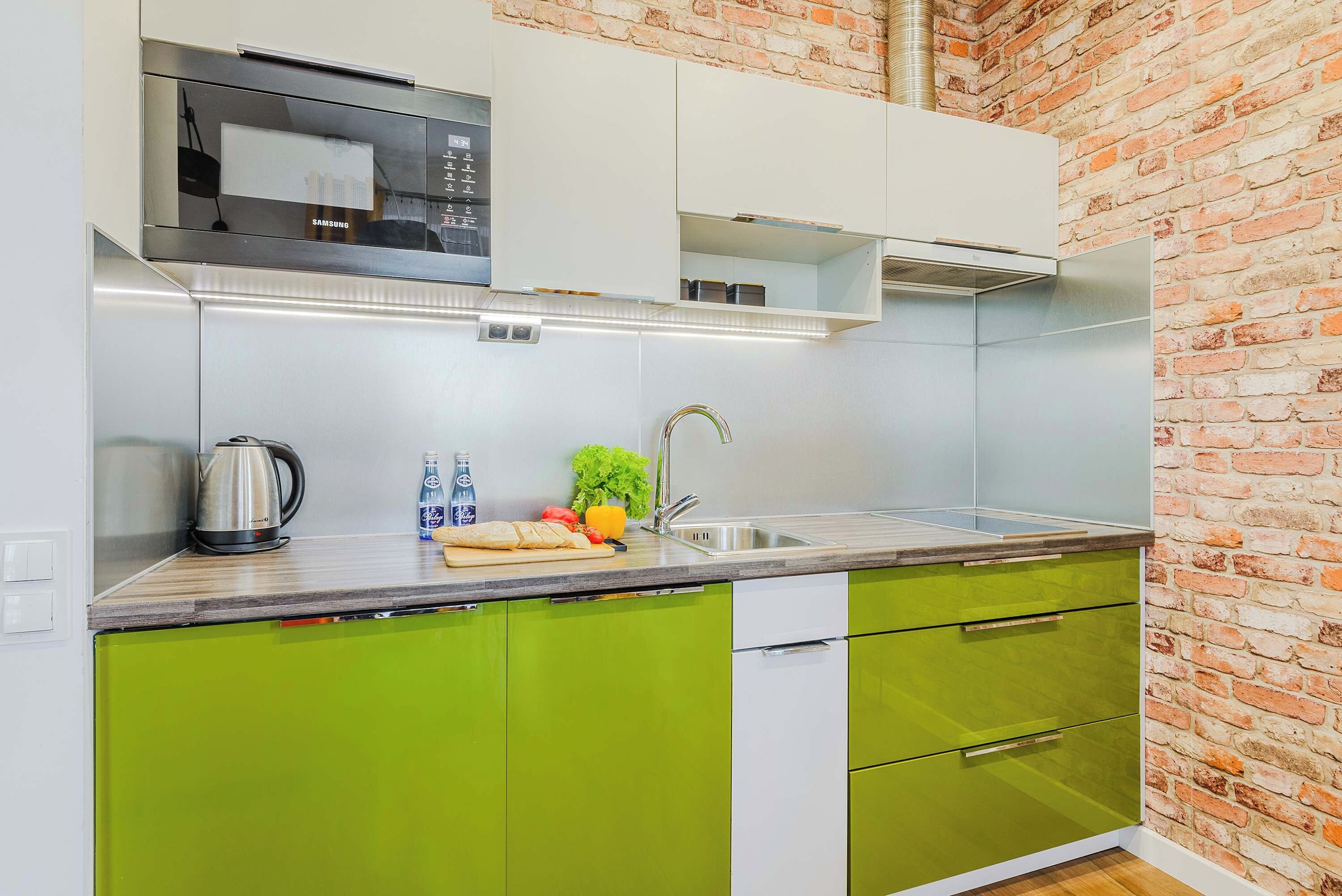 A modern kitchen with green cabinets, a stainless steel sink, and a built-in microwave.