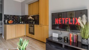 A modern kitchen with wooden cabinets, a black tiled backsplash, and a large flat-screen TV displaying the Netflix logo. - Lumina lux apartment in Warsaw (Warszawa BIG)