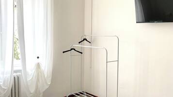 A hotel room with a bed, a wall-mounted TV, a drying rack, and sheer curtains.