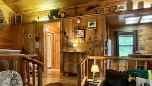 Interno di una baita in legno con una scala, un divano in pelle e un'area pranzo.