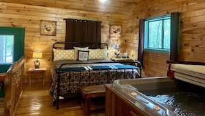 Camera da letto in una casetta di legno, con un letto, un comodino, una lampada, una finestra e una vasca idromassaggio.