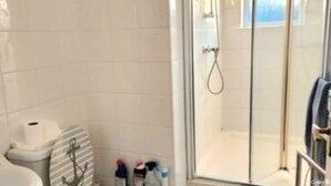 A bathroom with white tiles, a glass shower enclosure, a toilet, and a sink. - Ashford Cozy Apartment in Town Centre (Ashford)