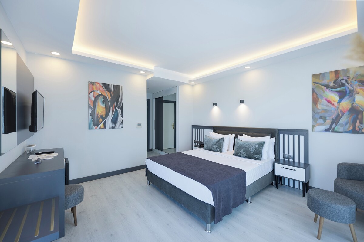 A modern bedroom with a large bed, bedside tables, a desk, and artwork on the walls.