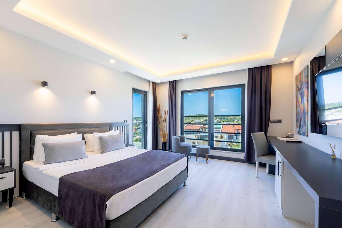 A modern hotel room with a large bed, a desk, and a view of the city.