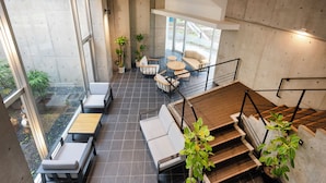 A spacious indoor area with a modern design, featuring a seating area with sofas and tables, a staircase, and potted plants. - Satonuma Resort Hotel Komorinu (Tatebayashi)