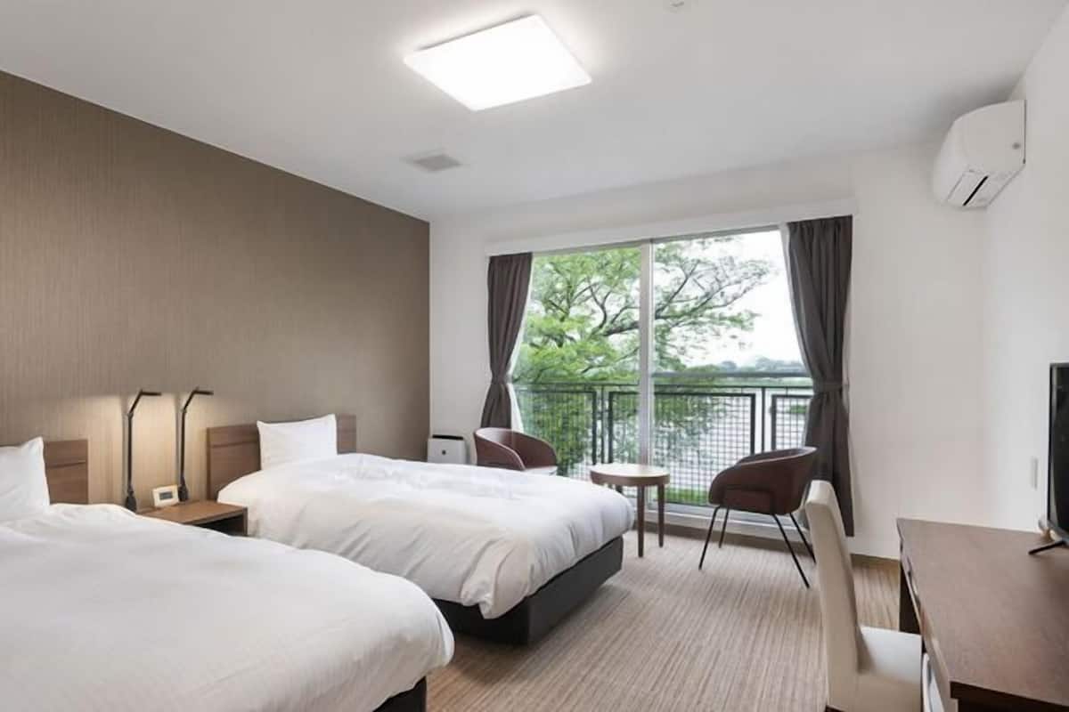 Habitación de hotel con dos camas, un escritorio, una silla, un televisor y un balcón con vistas.