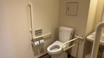 A standard bathroom with a toilet, a handrail, a toilet paper holder, and a sink.