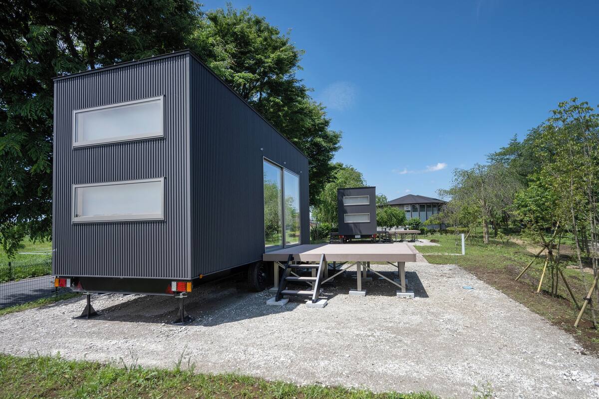 Uma casa móvel moderna e compacta, com teto plano, janelas amplas e uma pequena estrutura anexa.