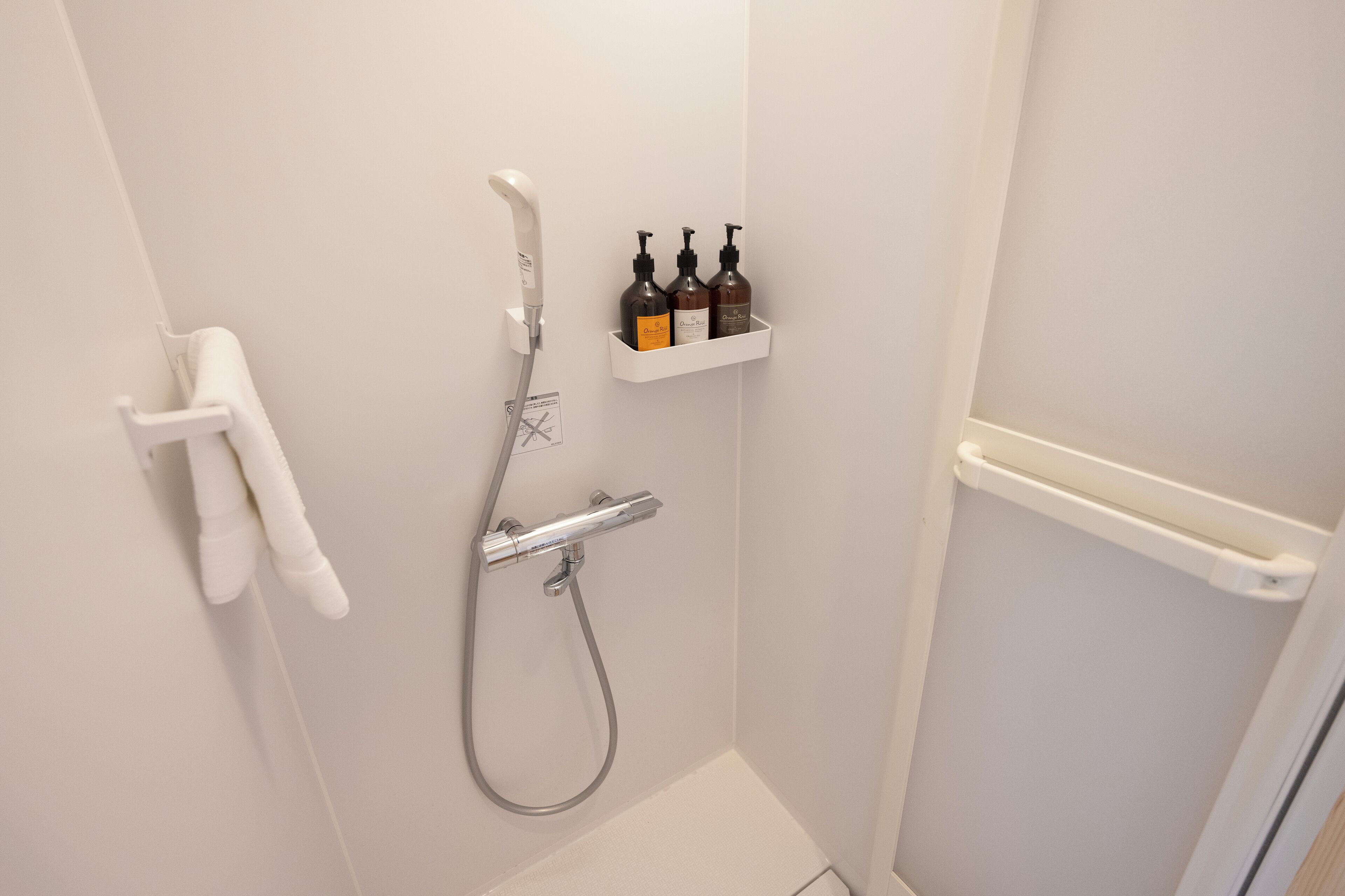 Un baño con ducha, toallero y estante con artículos de aseo.