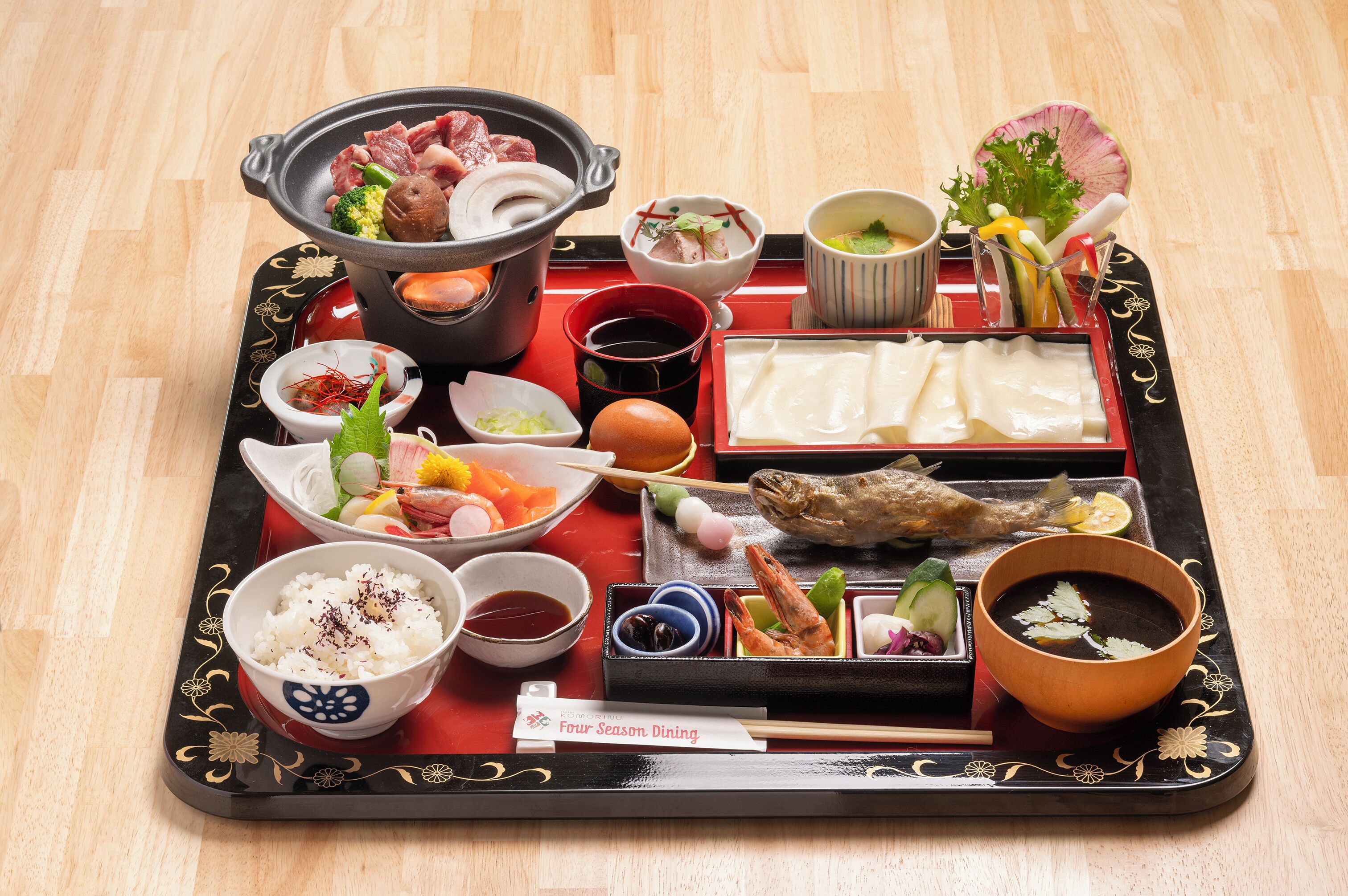A tray with various Japanese dishes including sushi, sashimi, and a hot pot.