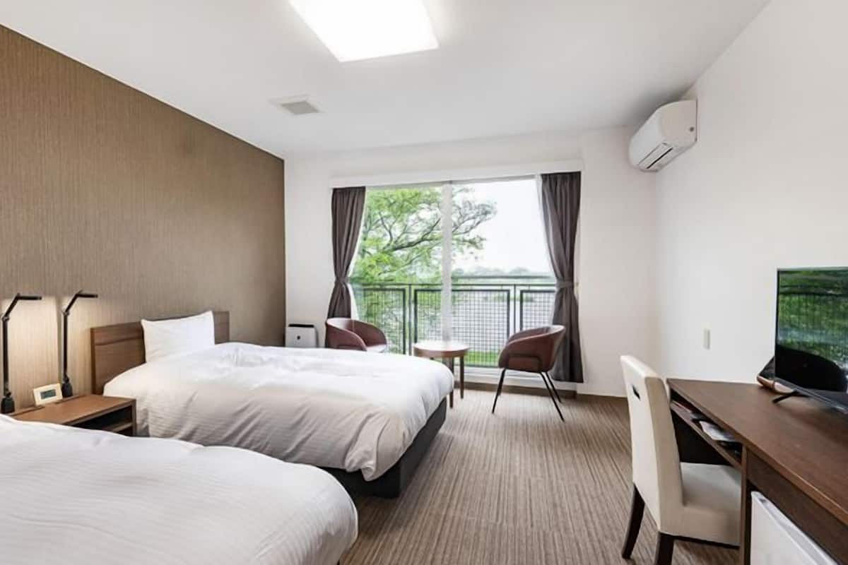 Habitación de hotel con dos camas, un escritorio, una silla, un televisor y un balcón con vistas.