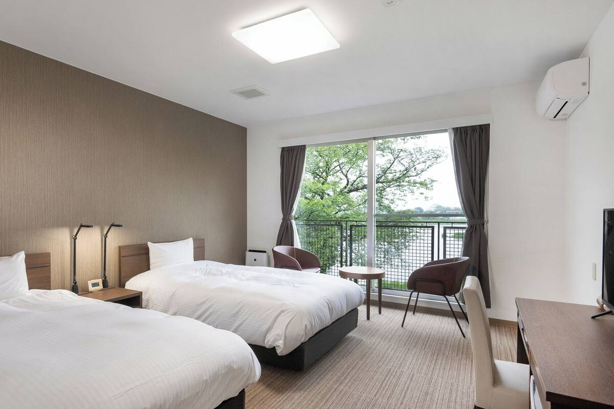Quarto de hotel com duas camas, uma mesa, uma cadeira, uma televisão e vista para a água.