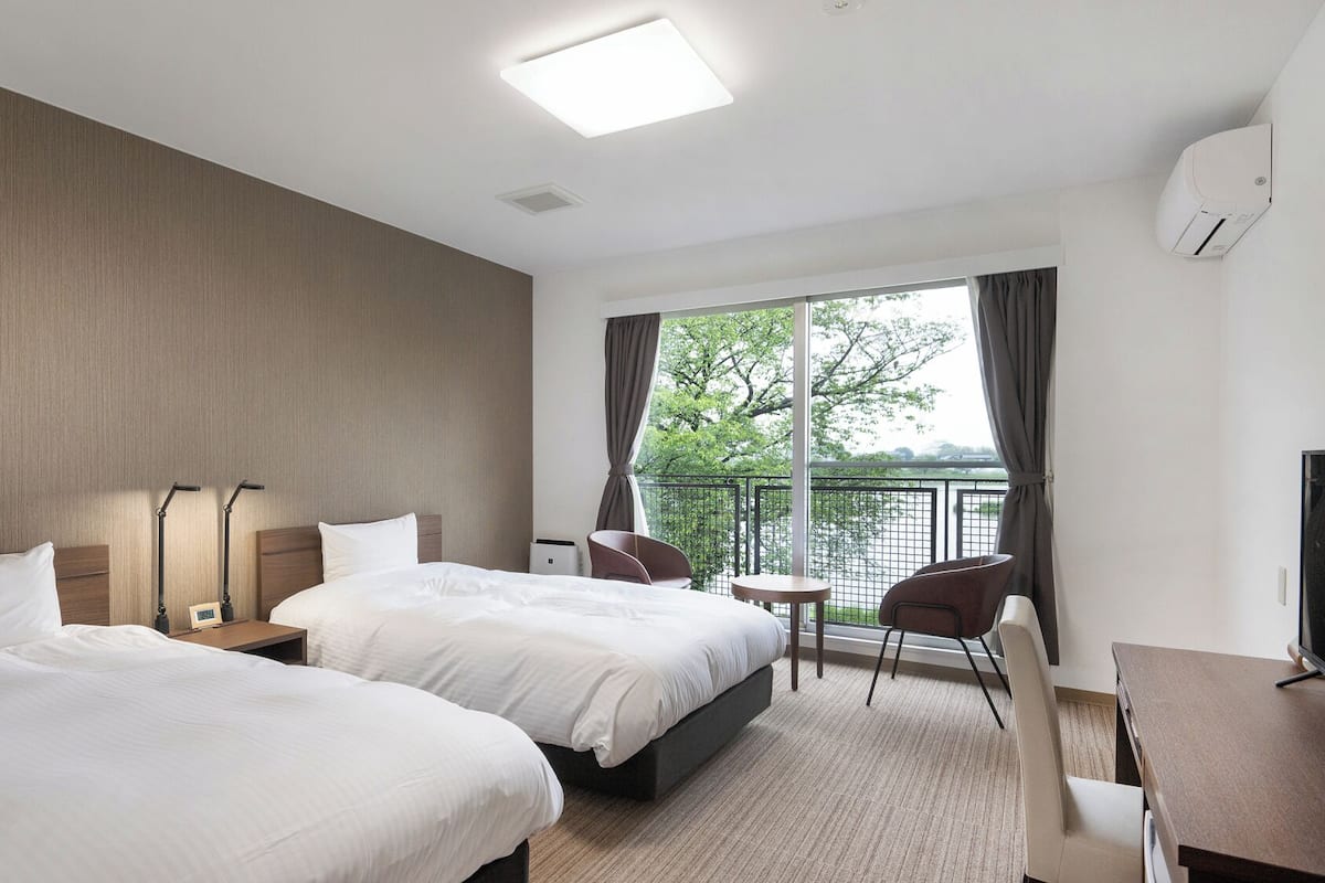 Une chambre d’hôtel avec deux lits, un bureau, une chaise, une télévision et une vue sur une étendue d’eau.