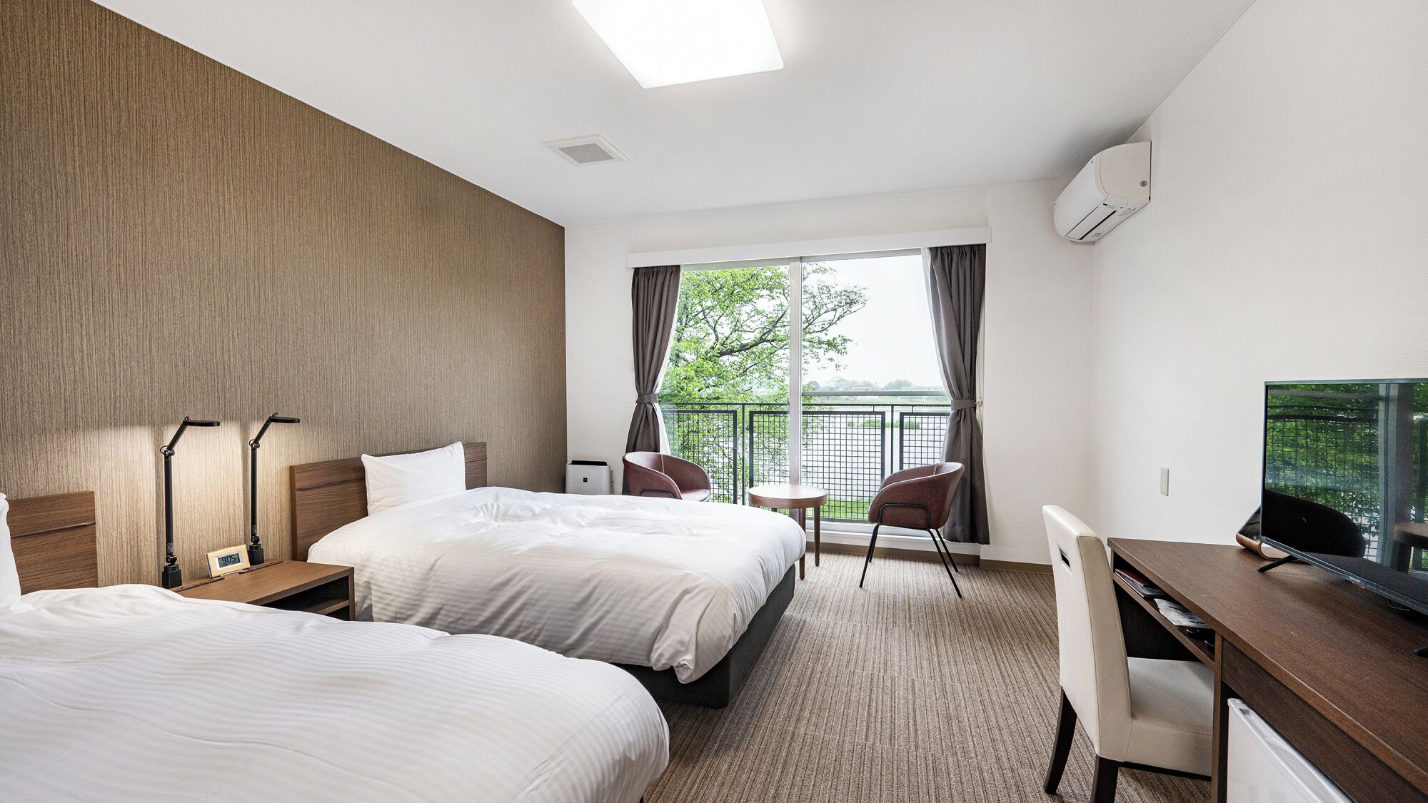 Une chambre d’hôtel avec deux lits, un bureau, une chaise, une télévision et un balcon avec vue.