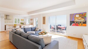 Un salon moderne avec un canapé gris, une petite table ronde et une grande fenêtre donnant sur la mer.