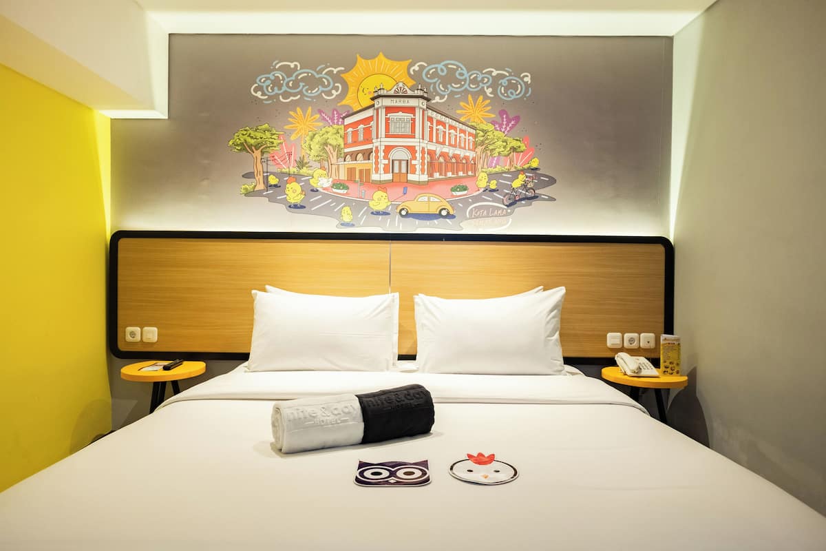 Une chambre d’hôtel avec un lit, deux oreillers, une table de chevet avec un téléphone et une œuvre d’art murale représentant un bâtiment.