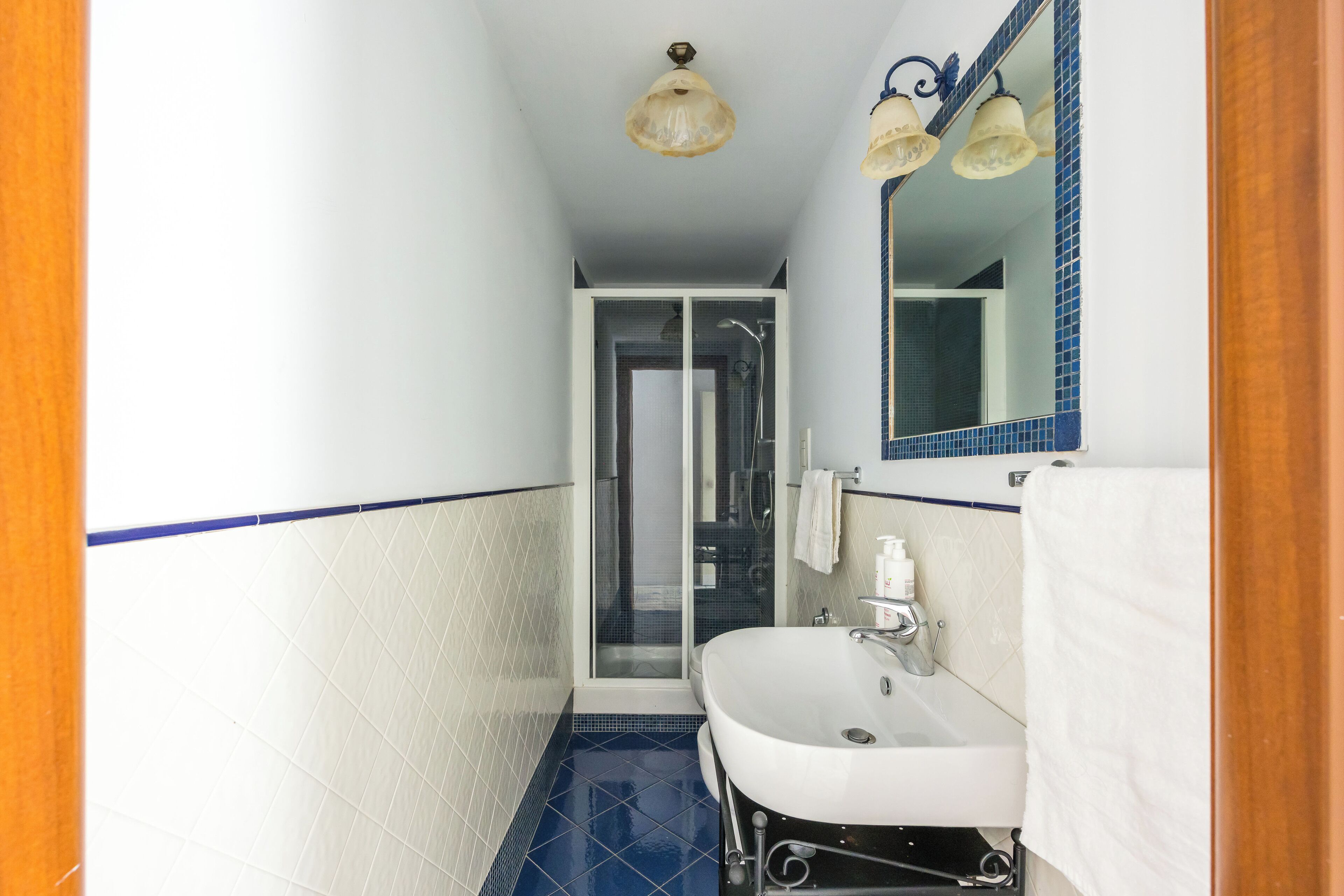 Une petite salle de bain avec un lavabo blanc, un sol carrelé de bleu et une porte de douche en verre.