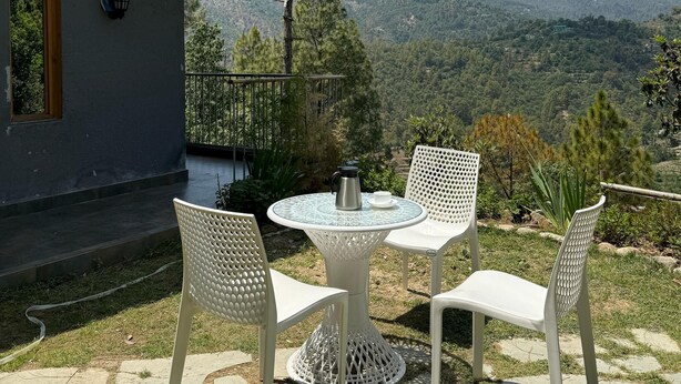 A terrace with two white chairs and a table, overlooking a mountainous landscape. - Rasberry Homes (Dhari)
