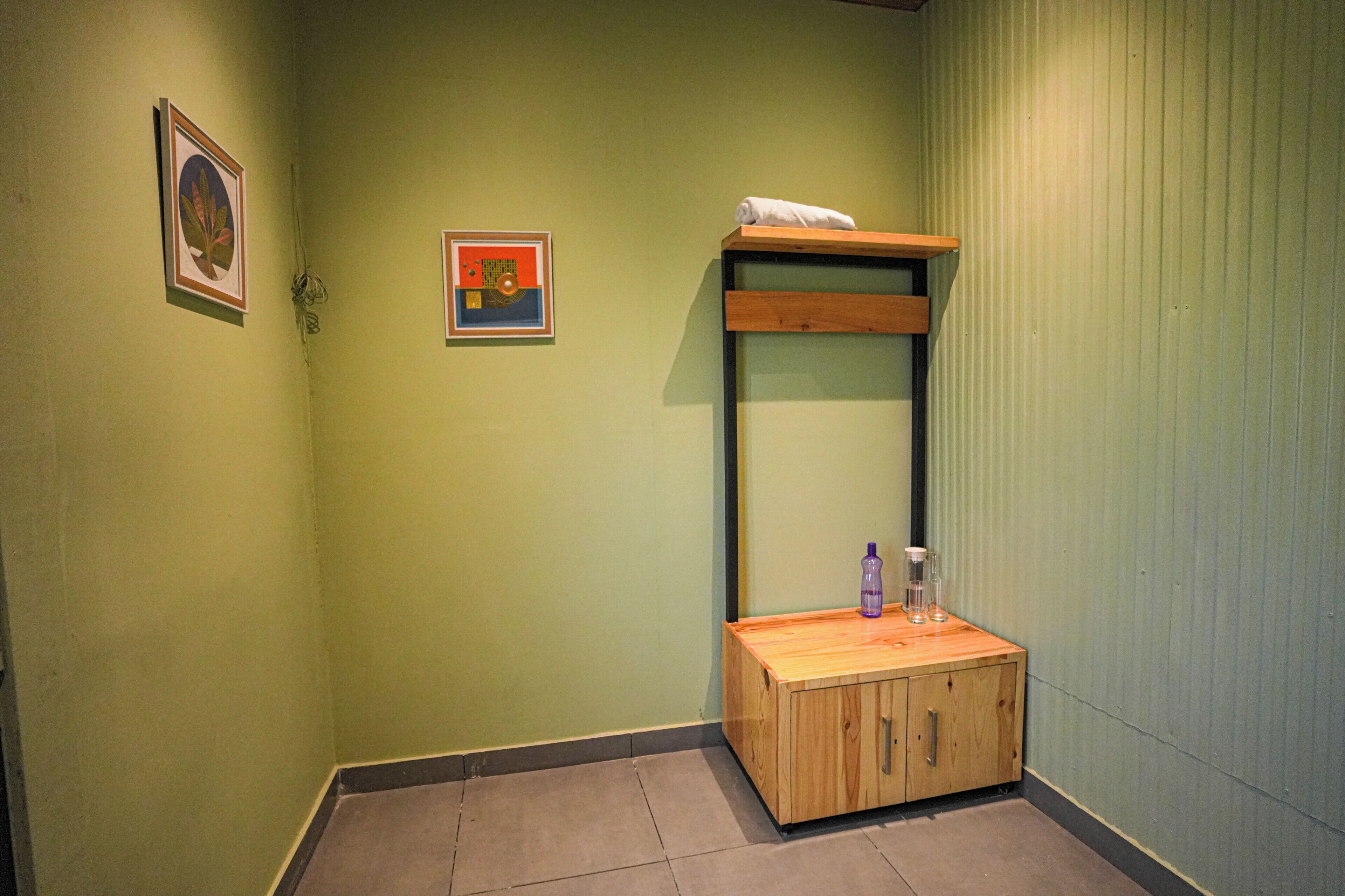 Una habitación con literas, un pequeño armario de madera y dos cuadros en la pared.