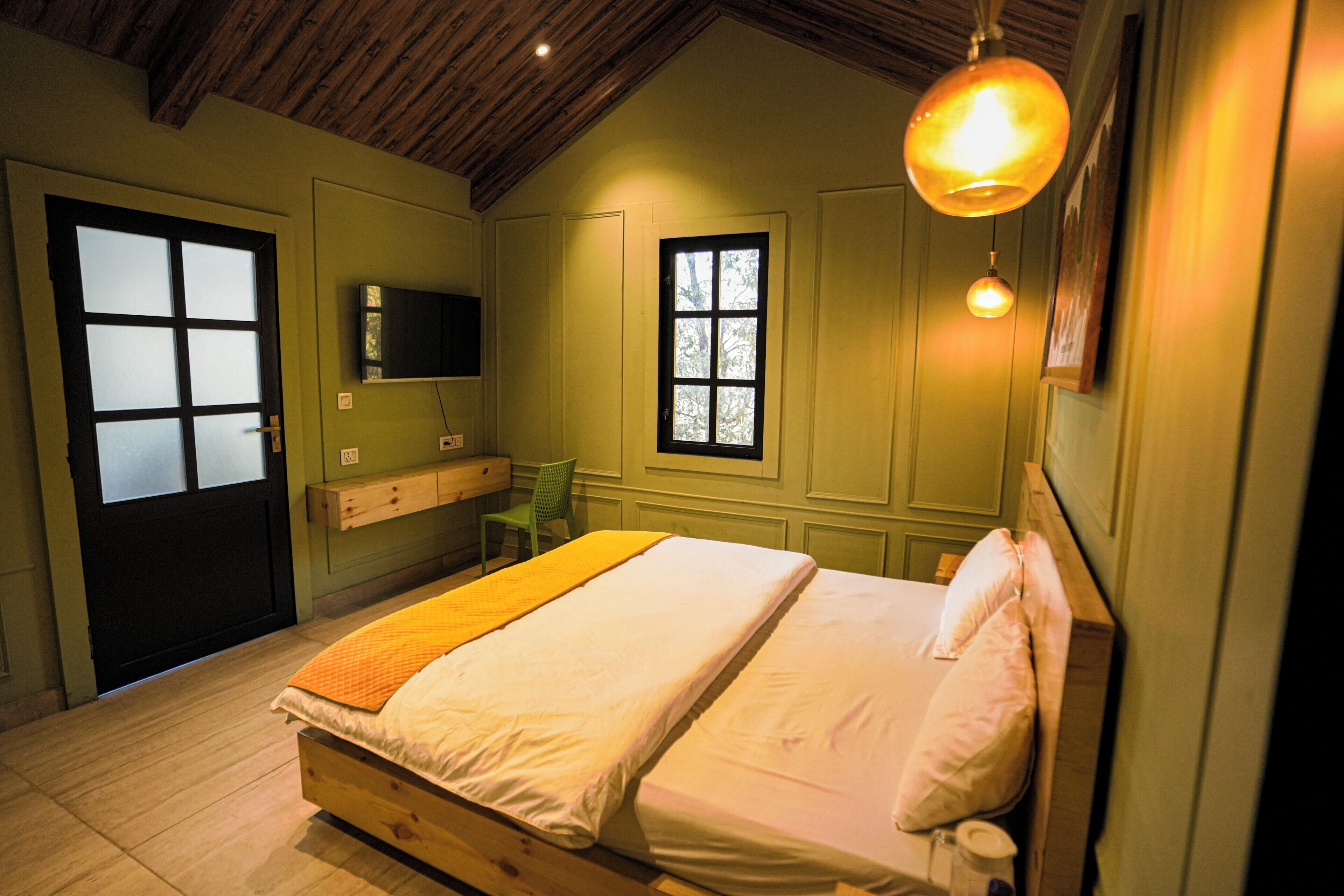 A bedroom with a wooden bed, a bedside table, a chair, a window, and a wall-mounted TV.