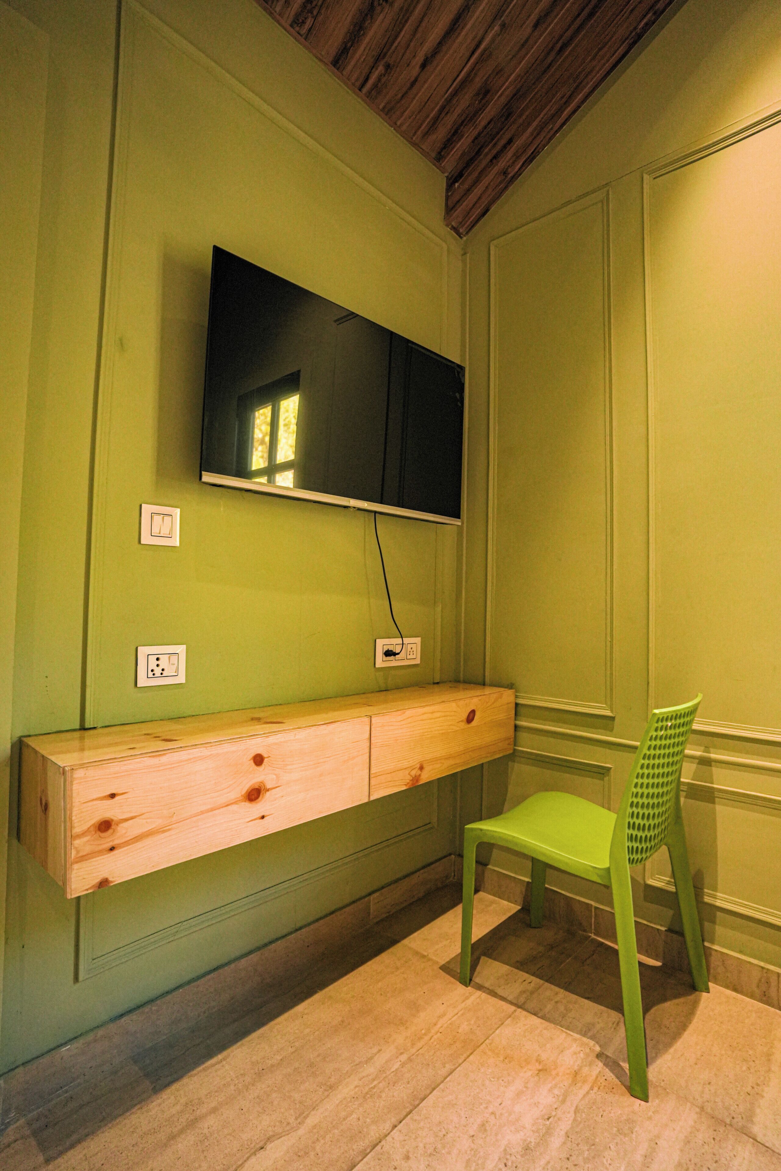 Una habitación con un banco de madera, una silla verde, un televisor de pantalla plana montado en la pared y un techo de madera.