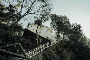 A white building with a staircase leading up to it, surrounded by trees. - Rasberry Homes (Dhari)